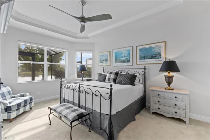 Bedroom with ceiling fan, light colored carpet, crown molding, and a tray ceiling