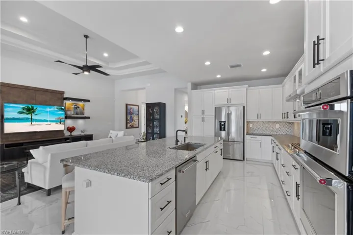 Kitchen with light tile patterned flooring, white cabinetry, stainless steel appliances, sink, and a center island with sink