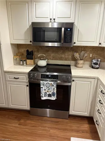 Kitchen with electric stove, decorative backsplash, white cabinetry, and light stone countertops