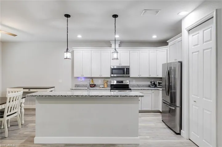 Kitchen featuring stainless steel appliances, white cabinetry, an island with sink, light wood-type flooring, and pendant lighting