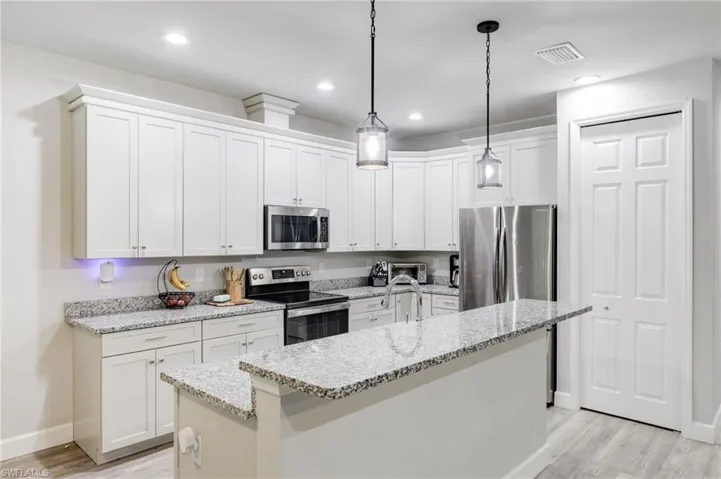 Kitchen with an island with sink, light hardwood / wood-style flooring, decorative light fixtures, and appliances with stainless steel finishes