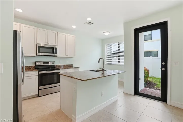 Kitchen with stainless steel appliances, dark stone countertops, recessed lighting, a kitchen island with sink, and white cabinetry