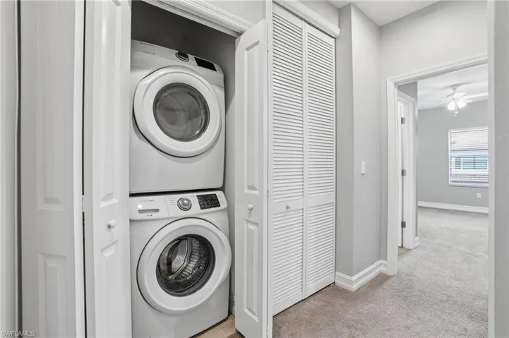 Laundry room featuring light carpet, stacked washing machine and dryer, and ceiling fan