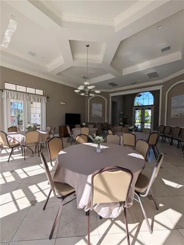 Tiled dining space with a chandelier, healthy amount of natural light, ornamental molding, coffered ceiling, and french doors