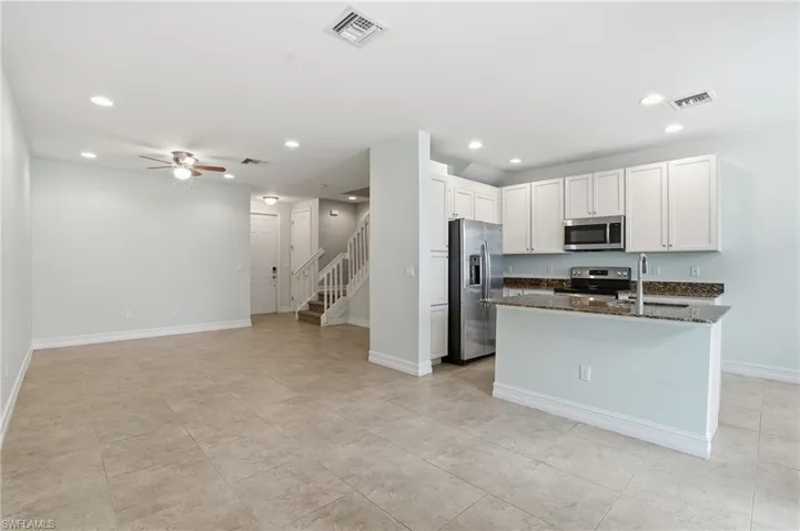Kitchen with dark stone counters, white cabinetry, stainless steel appliances, open floor plan, and recessed lighting