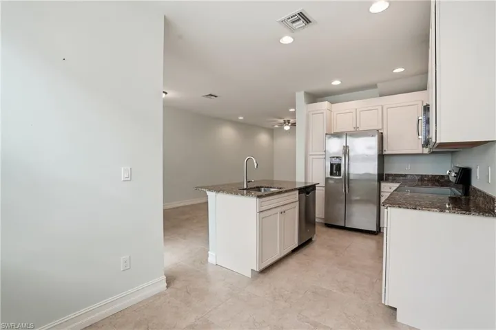 Kitchen with dark stone counters, appliances with stainless steel finishes, a center island with sink, recessed lighting, and a ceiling fan