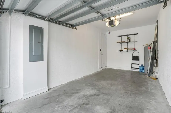 Garage featuring electric panel, water heater, a garage door opener, and a textured wall