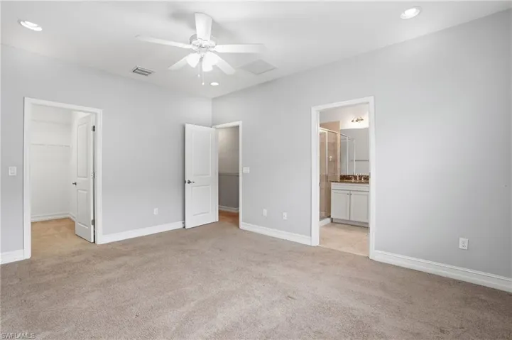 Unfurnished bedroom featuring light carpet, a walk in closet, ceiling fan, ensuite bath, and recessed lighting