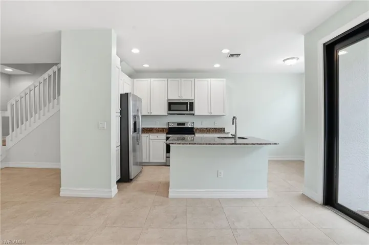 Kitchen with dark stone countertops, white cabinets, stainless steel appliances, a kitchen island with sink, and recessed lighting