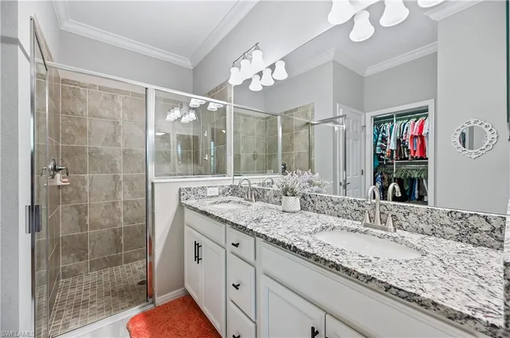 Bathroom featuring ornamental molding, a shower with shower door, and double sink vanity