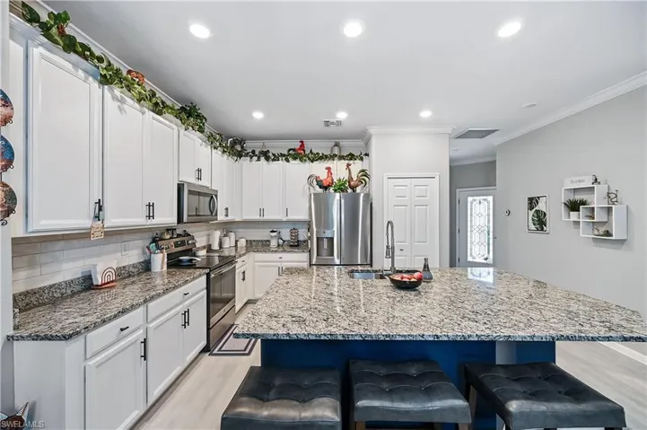 Kitchen with light hardwood / wood-style floors, backsplash, a center island with sink, white cabinetry, and appliances with stainless steel finishes