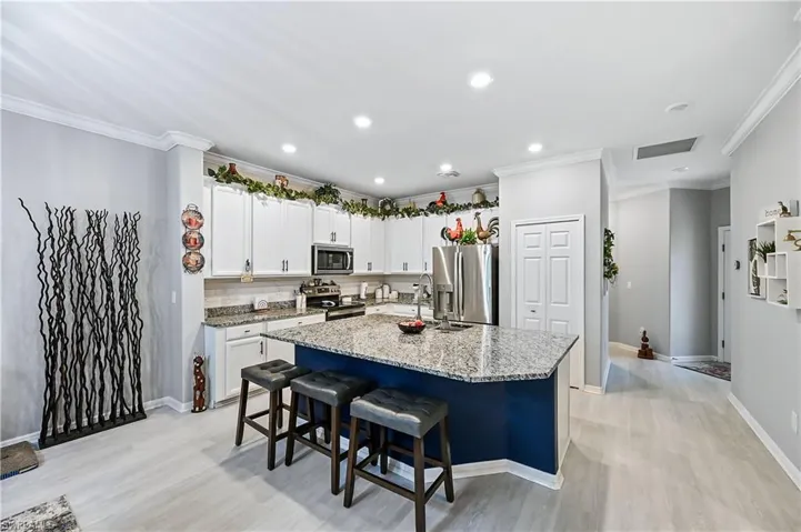 Kitchen featuring a center island with sink, white cabinetry, light stone countertops, appliances with stainless steel finishes, and a breakfast bar