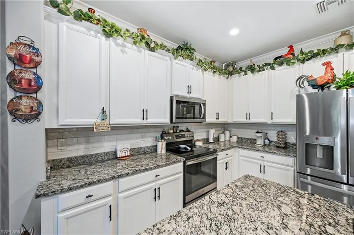 Kitchen with light stone countertops, stainless steel appliances, tasteful backsplash, and white cabinetry