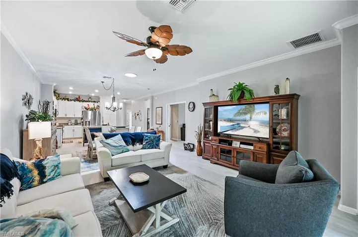 Living room featuring wood-type flooring, ornamental molding, and ceiling fan with notable chandelier