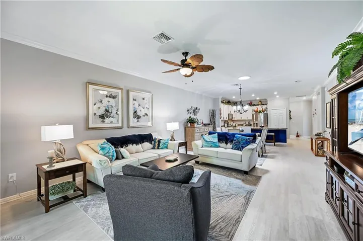 Living room with ornamental molding, light hardwood / wood-style floors, and ceiling fan with notable chandelier
