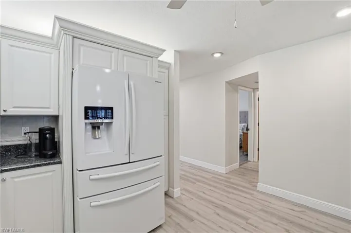 Kitchen with white refrigerator with ice dispenser, white cabinetry, dark stone counters, a ceiling fan, and light wood-type flooring