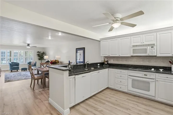 Kitchen with a ceiling fan, open floor plan, white appliances, and white cabinets