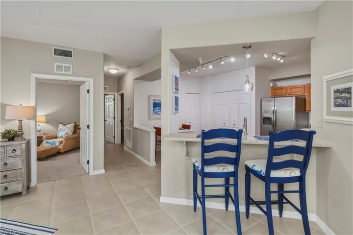 Kitchen pass-through breakfast bar with light-toned countertop, pendant lighting, track lighting, and stainless steel appliances
