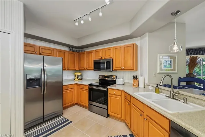 Kitchen featuring stainless steel appliances, wood cabinetry, stone countertops, a double basin sink, and tile flooring