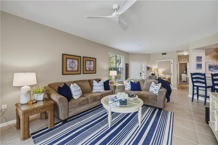 Spacious living area featuring light-toned walls, a white ceiling fan, and large windows providing natural light