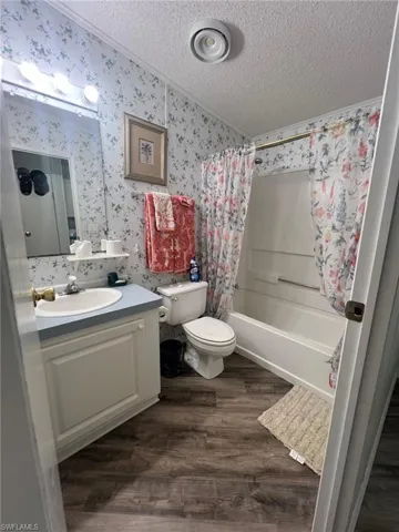 Full bathroom with hardwood / wood-style floors, vanity, shower / bath combination with curtain, toilet, and a textured ceiling