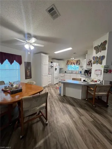 Kitchen with white cabinetry, white refrigerator with ice dispenser, kitchen peninsula, hardwood / wood-style floors, and a textured ceiling