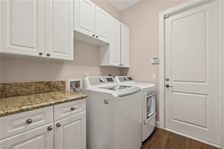 Clothes washing area with cabinets, washing machine and clothes dryer, and dark hardwood / wood-style flooring