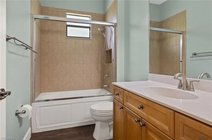 Full bathroom with vanity, wood-type flooring, shower / bath combination with glass door, and toilet