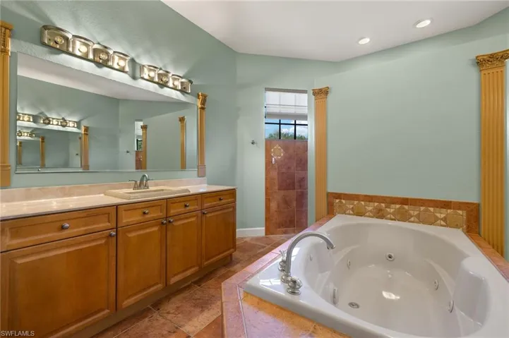 Bathroom with tiled tub, vanity, and tile patterned flooring