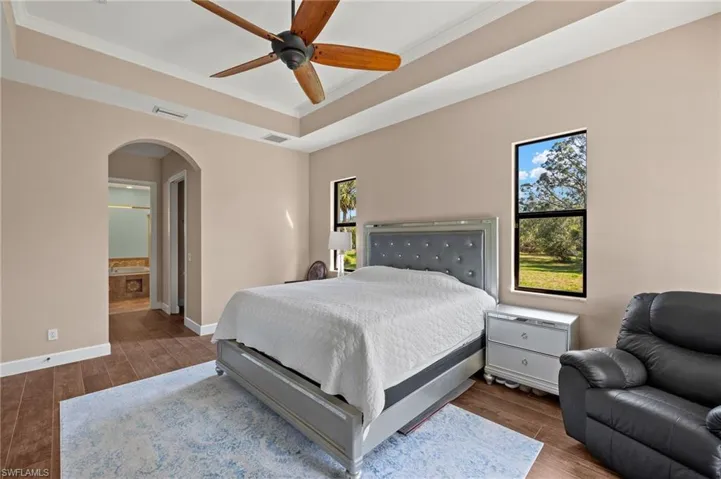 Bedroom featuring crown molding, a tray ceiling, dark wood-type flooring, and ceiling fan