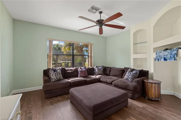 Living room featuring dark wood-type flooring, ceiling fan, and built in shelves