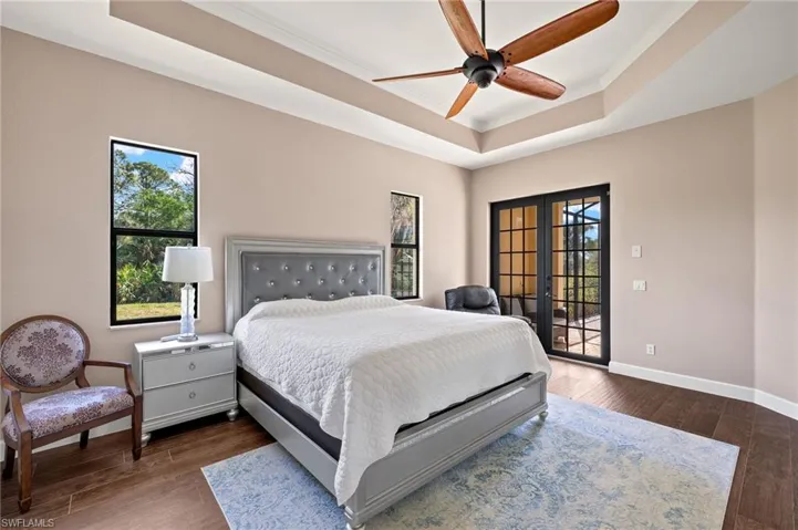 Bedroom with dark wood-type flooring, access to exterior, a tray ceiling, ornamental molding, and french doors