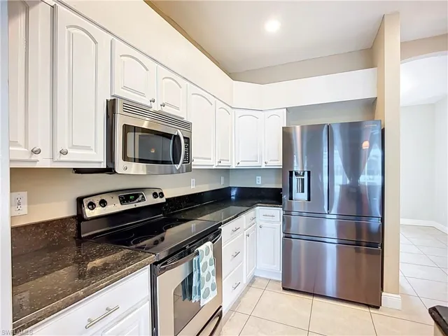 Kitchen with stainless steel appliances, light tile patterned floors, dark stone counters, and white cabinets