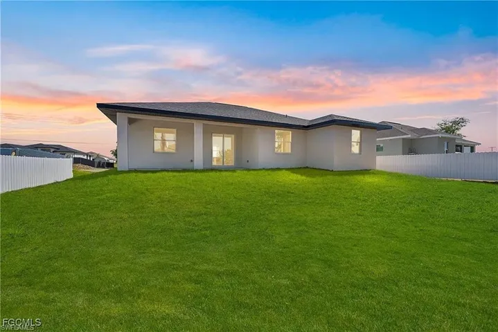 Expansive rear yard featuring a vast green lawn, white picket fencing, and a stucco exterior