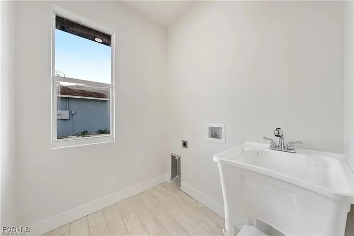 Utility sink featuring a chrome faucet, light wood-finish flooring, white baseboards, and a single-pane window