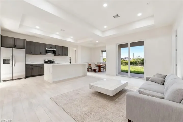 Open-concept living area featuring light-toned flooring, recessed lighting, and a tray ceiling