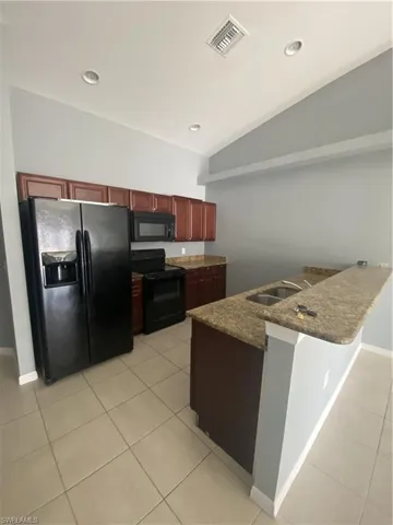 Kitchen with refrigerator, light tile patterned floors, black range, a peninsula, and lofted ceiling