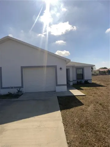 Ranch-style house with driveway, stucco siding, an attached garage, and a front lawn