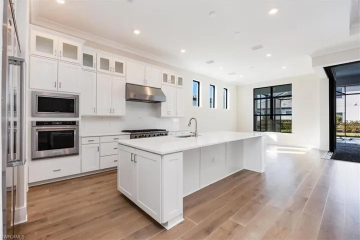 Kitchen with ornamental molding, built in appliances, white cabinets, under cabinet range hood, and a kitchen island with sink