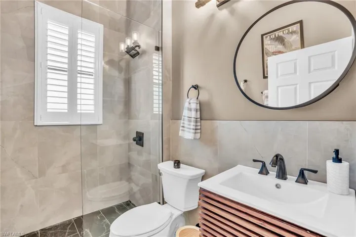 Bathroom with tile walls, toilet, vanity, and an enclosed shower