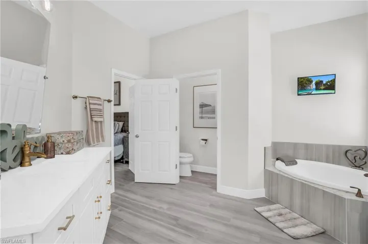 Bathroom featuring vanity, tiled bath, toilet, and hardwood / wood-style floors