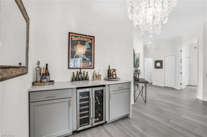Bar featuring gray cabinets, a notable chandelier, light hardwood / wood-style flooring, and wine cooler