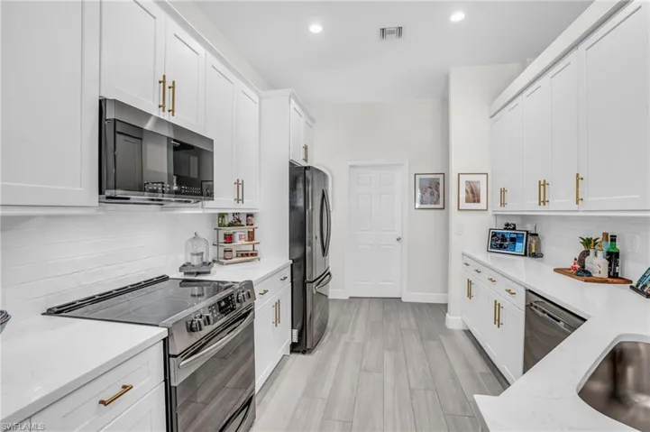 Kitchen with decorative backsplash, light stone counters, stainless steel appliances, and white cabinets