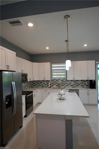 Kitchen featuring appliances with stainless steel finishes, white cabinets, hanging light fixtures, tasteful backsplash, and light tile patterned flooring