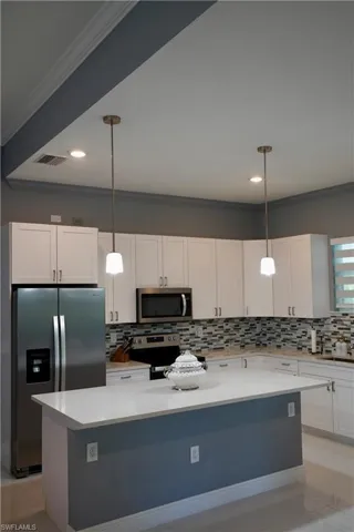 Kitchen with crown molding, white cabinetry, backsplash, appliances with stainless steel finishes, and light stone countertops