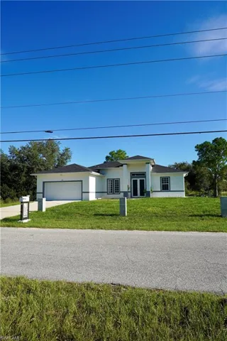 View of front facade with stucco siding, a front yard, an attached garage, and driveway