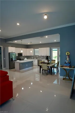 Kitchen with ornamental molding, backsplash, white cabinets, hanging light fixtures, and a kitchen island