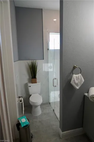Full bath with a marble finish shower, a textured wall, and light tile patterned floors