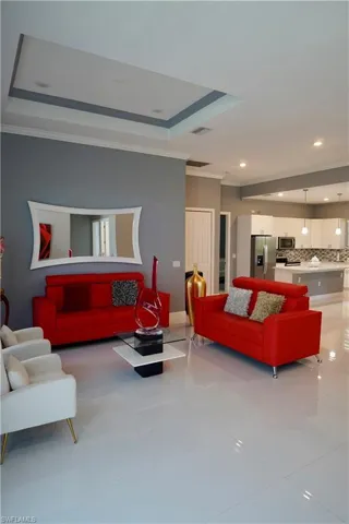 Living room featuring light tile patterned flooring, recessed lighting, a raised ceiling, and crown molding