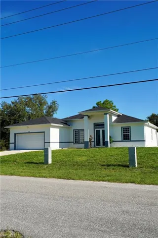 View of front of property with stucco siding, an attached garage, a front lawn, and driveway